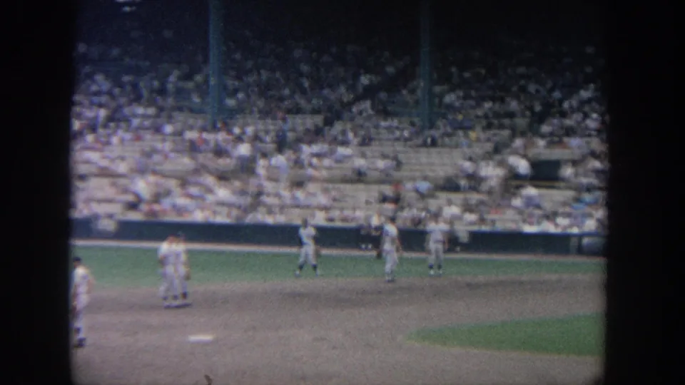 Soft 8mm view of players on the dirt infield and outfield edge, backed by crowded stadium seating in New York metadata.
