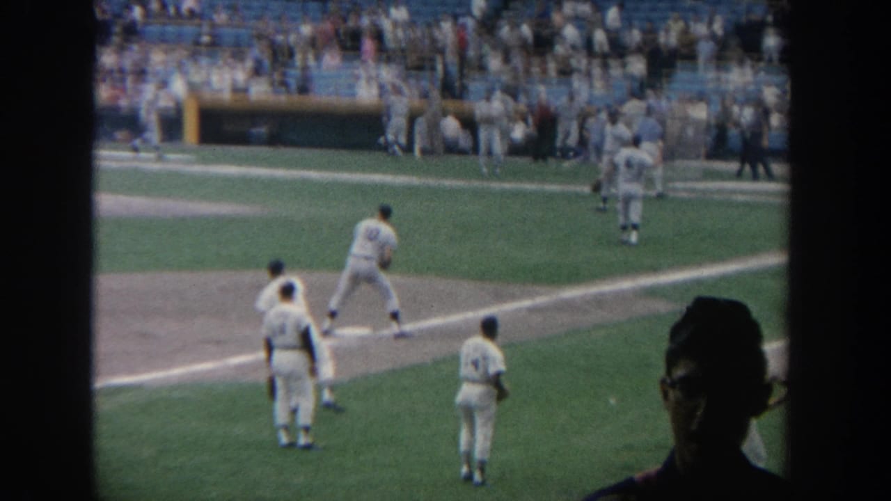 1964 New York 8mm footage shows baseball players in white uniforms practicing throws near the infield before a game.