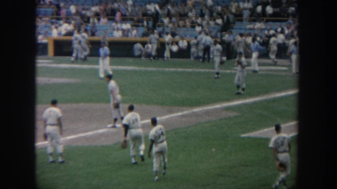 1964 New York home-movie view of baseball players in white uniforms on a green stadium field with a packed crowd behind them.
