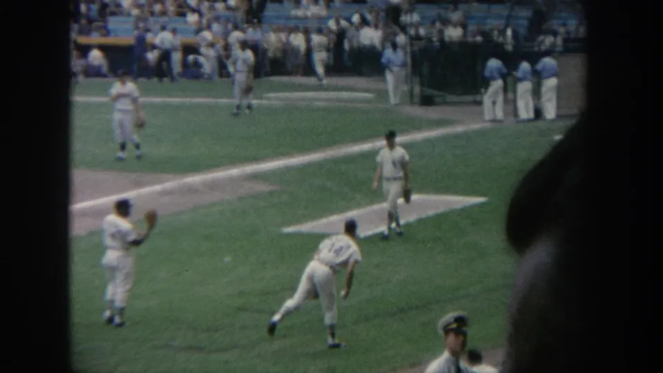 A 1964 New York stadium view shows players in white uniforms throwing on the field, with spectators seated in the background.