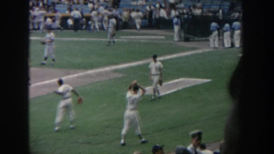 Home-movie footage from 1964 New York shows players warming up or moving between plays on a stadium field before a crowd.
