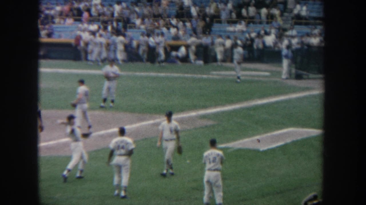 1964 New York baseball warm-up scene with uniformed players on the field and a crowded stadium visible beyond the infield.