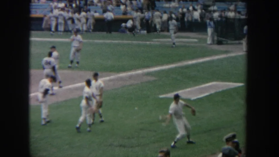 Uniformed baseball players appear to practice on a New York ballfield, with the dugout and stadium seating in the background.