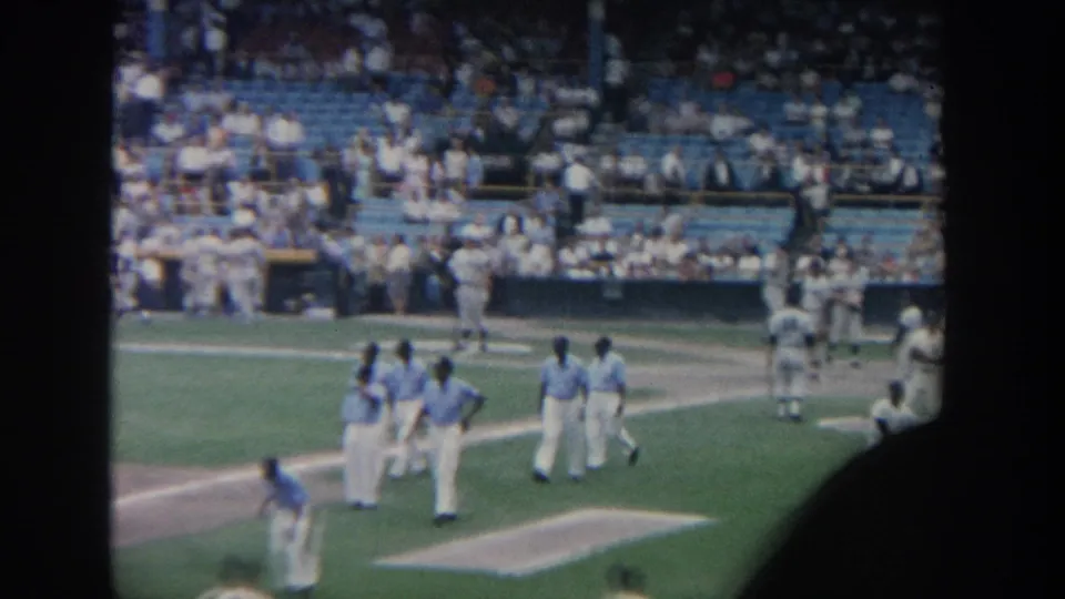 1964 New York stadium view with several baseball players gathered on the field and fans seated behind them.