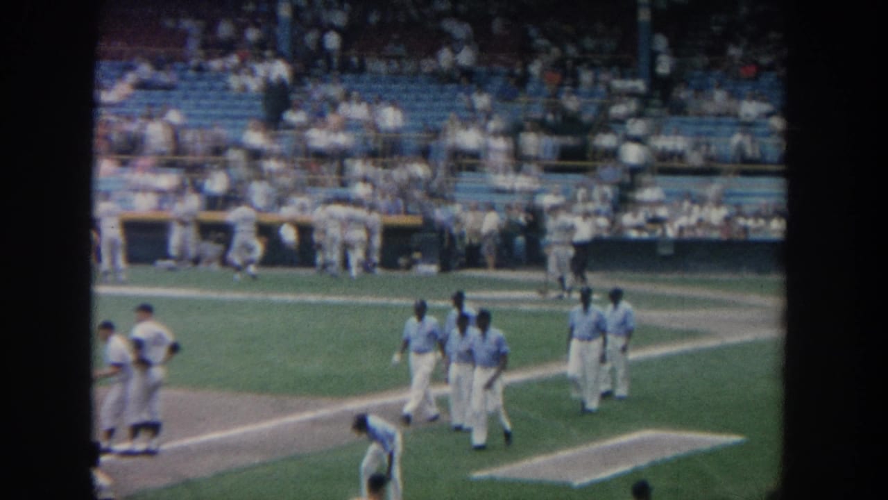 1964 New York 8mm footage appears to show baseball players in light uniforms walking across a stadium field before spectators.