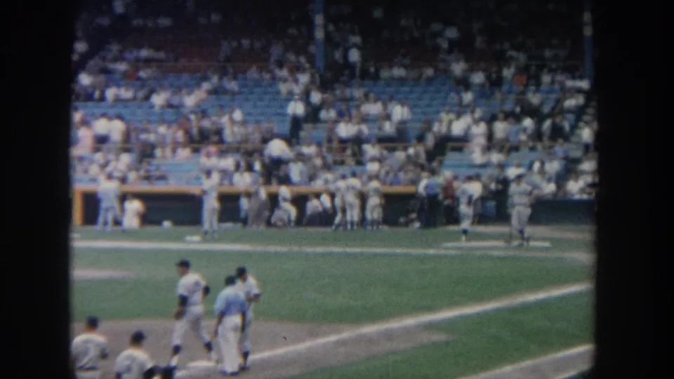 Home-movie view of a New York ballpark in 1964, showing players near the baseline and spectators in the stands.