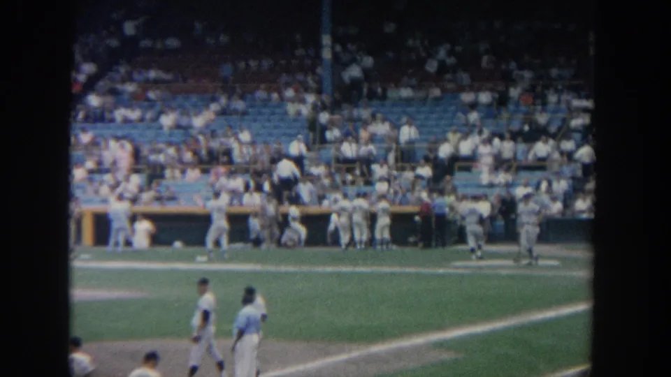 1960s New York stadium footage showing players on the field, dugout activity, and spectators across blue seats.