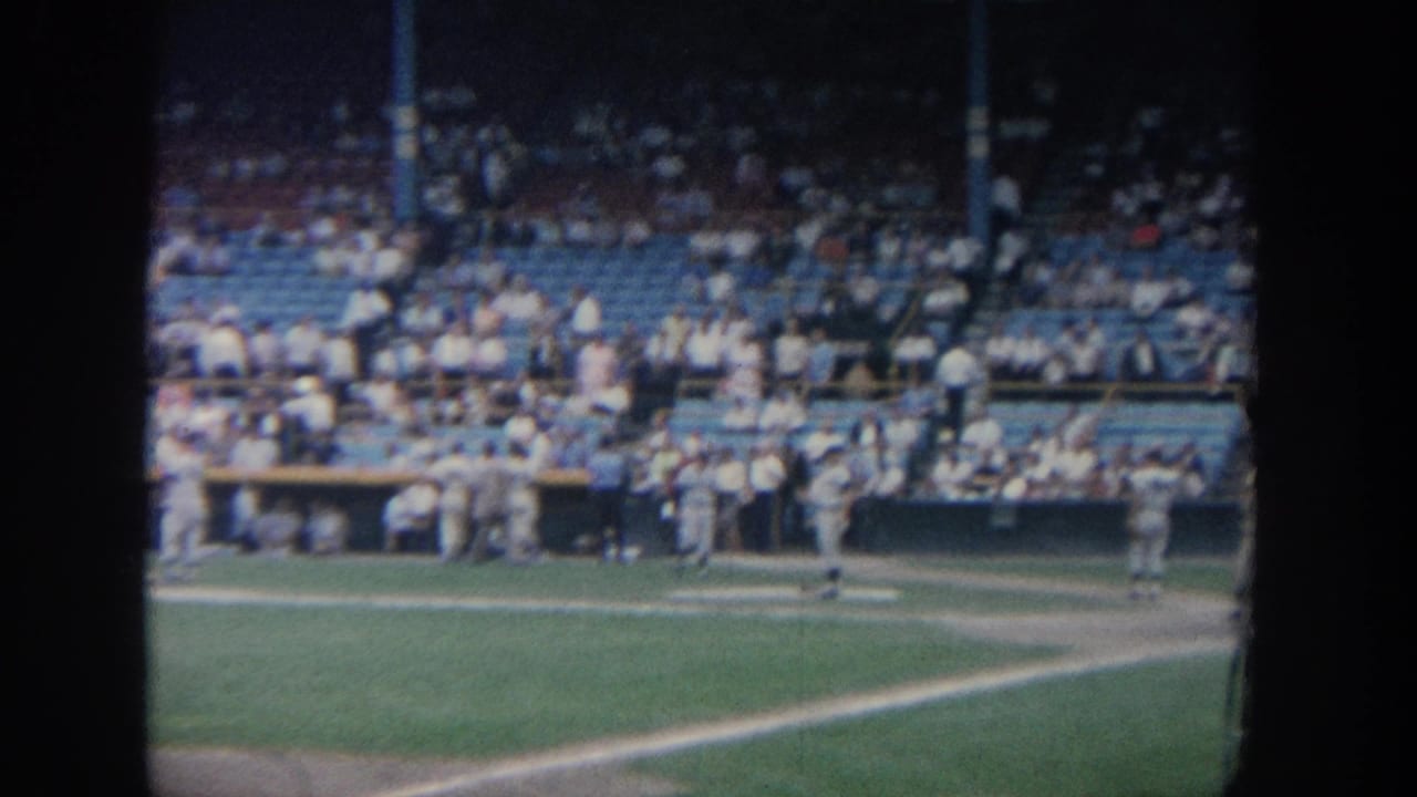 1964 New York 8mm footage shows baseball players near a dugout and a crowd in blue stadium seats.