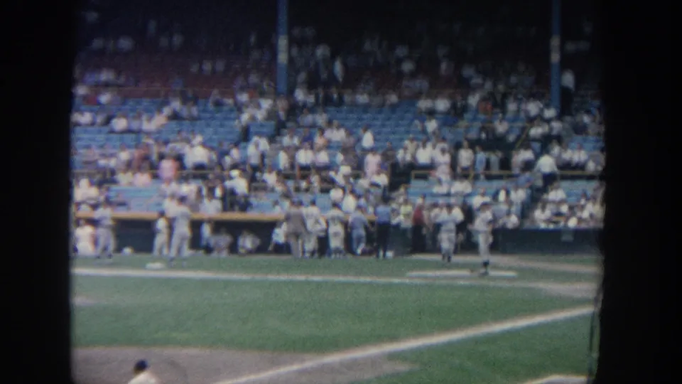 A distant 1964 New York stadium view shows baseball players near the dugout with spectators filling blue seats.