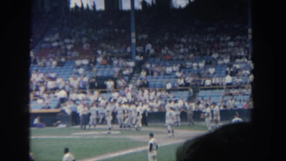 The final 1964 New York frame holds on players in white uniforms near the stands, with a crowded grandstand and arched roof openings visible.