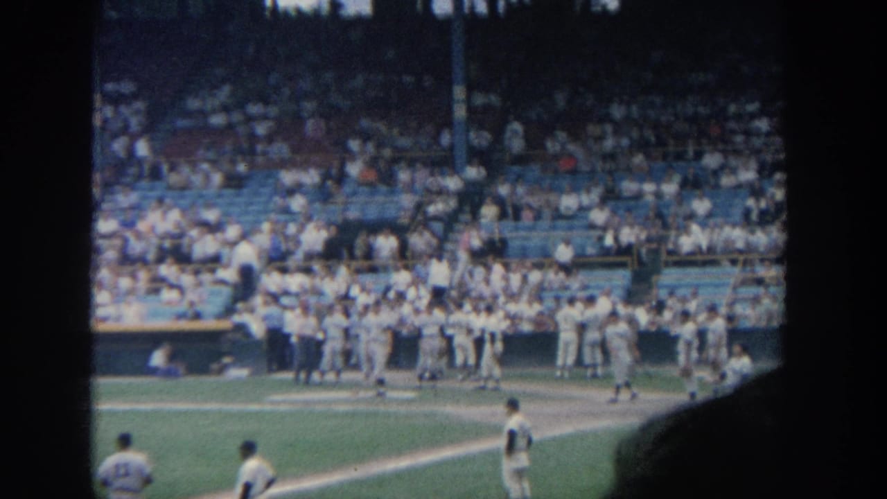 Players cluster near the dugout while a player stands on the field in front.