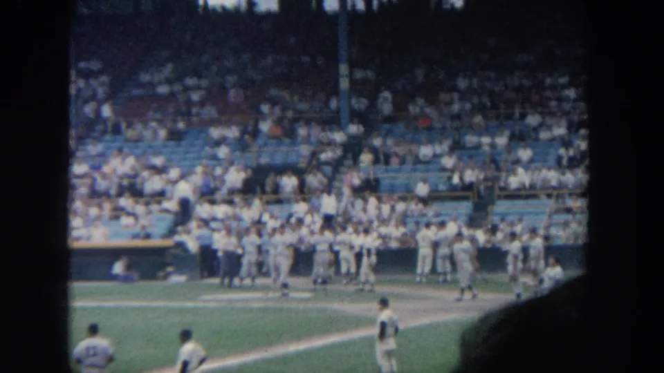 Spectator-shot 1964 New York baseball warm-up scene with players by the dugout and a crowded stand beyond.