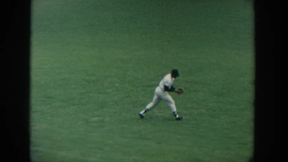 1964 New York home-movie frame of a white-uniformed outfielder bending into a warm-up motion on the grass.