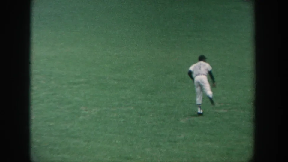 1964 New York 8mm frame showing an outfielder in a white uniform moving across the grass during warm-up.