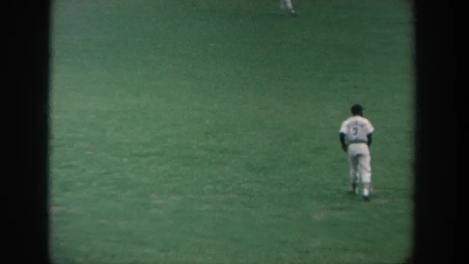 1964 New York 8mm frame showing a baseball player in a white uniform with number 3 standing on the outfield grass.