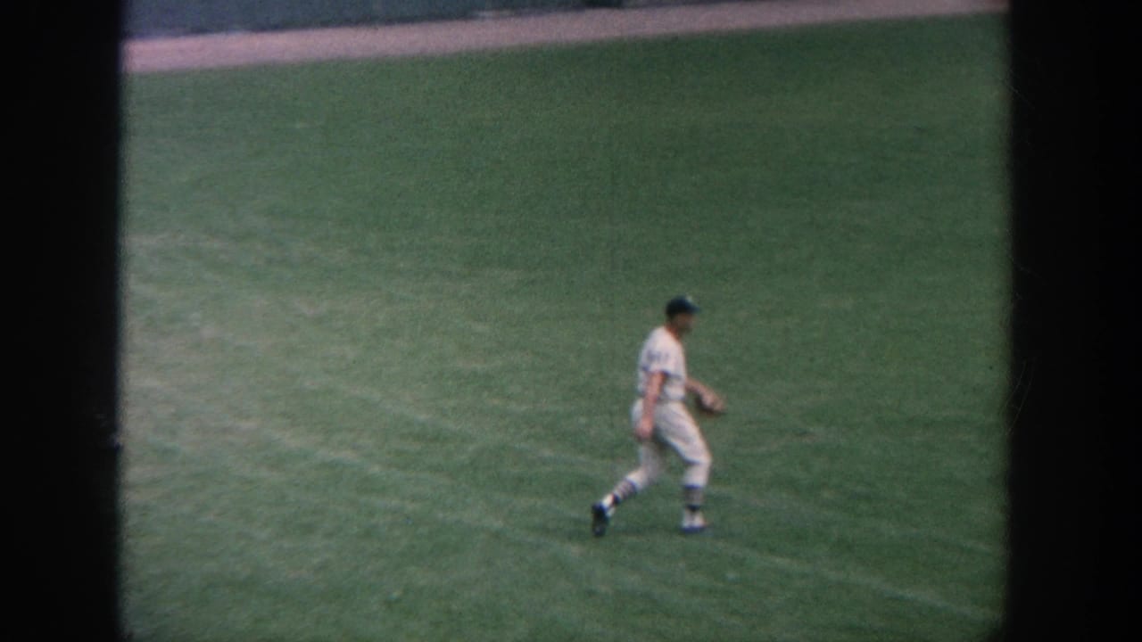Baseball player in a white uniform walks across the green outfield.