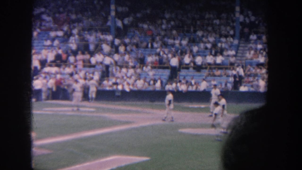 Baseball players on the field with home plate area, crowd seating, and a foreground head silhouette.