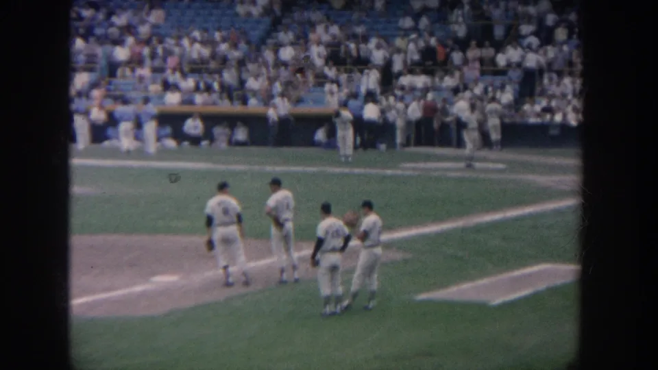 Group of baseball players near the infield at a packed 1964 New York stadium, with dugout area, blue seats, and crowd behind them.