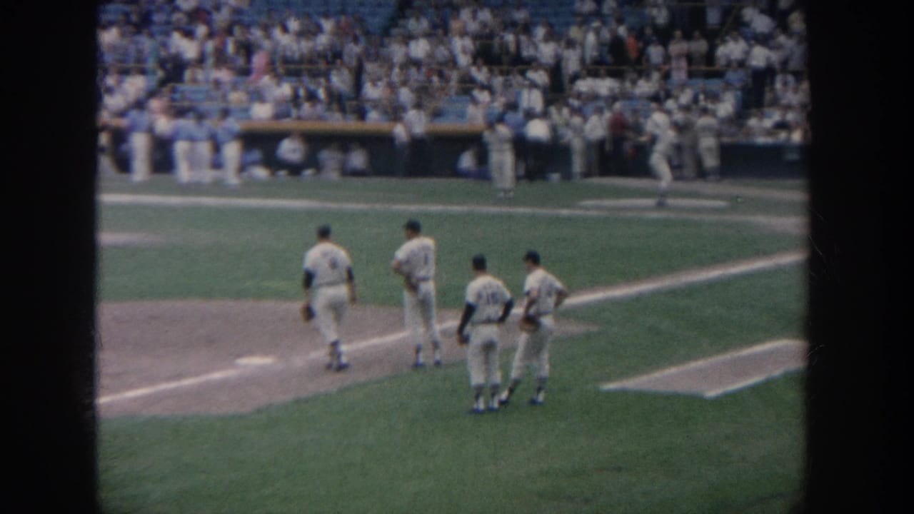 1964 New York baseball footage shows four players near first base as a large stadium crowd watches from the stands.