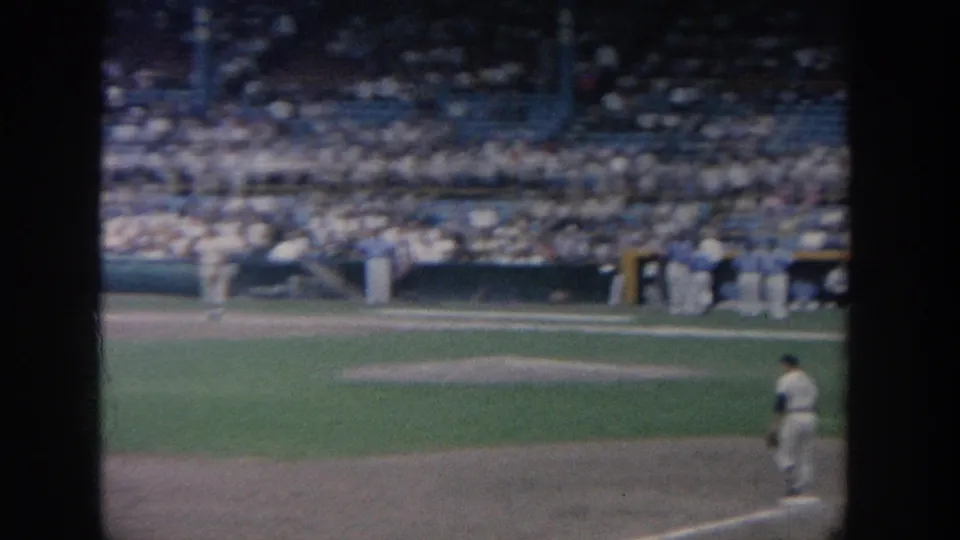 The 8mm frame looks across the baseball infield toward packed stands, with one player partially visible near the lower right.