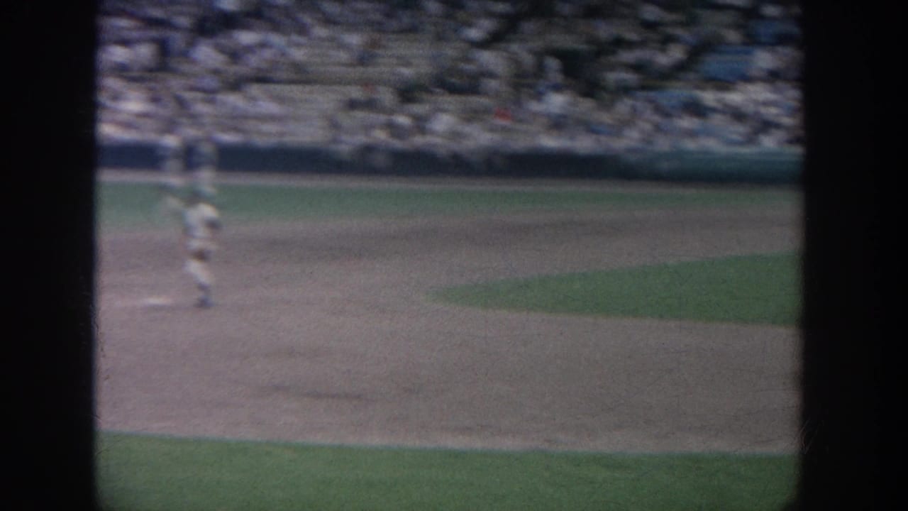 1964 New York baseball game footage showing the infield from a spectator angle, with a player at left and a crowded stand in the background.