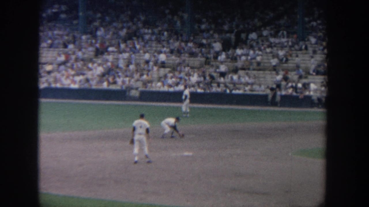 Infield player bends near the base while another player stands nearby and fans fill the stands.