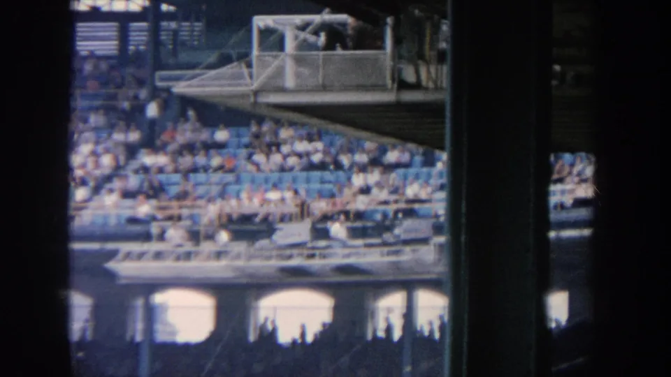 1964 New York baseball stadium view from the stands, showing seating tiers, spectators, and a raised platform or booth area.