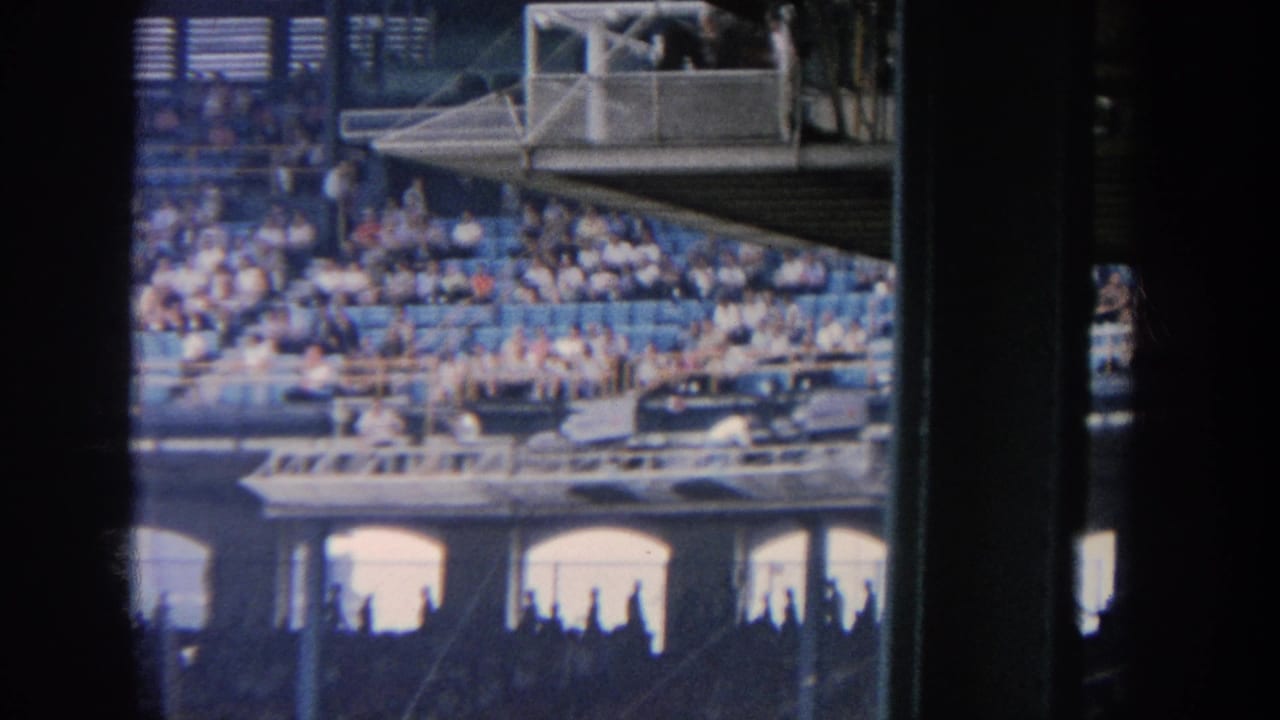 Similar stadium crowd view with blue seating, press structure and dark film-edge framing.