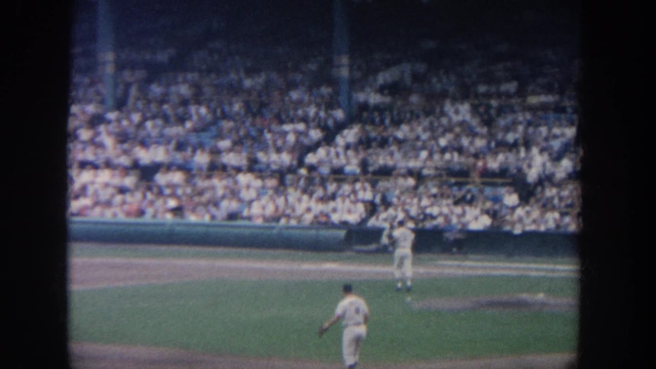 1964 New York home-movie frame showing baseball players on the field before a crowded stadium seating area.