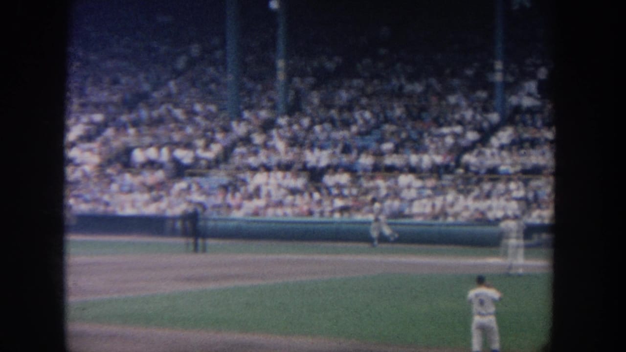 Ballpark view with a player near the right edge and spectators filling the stands.