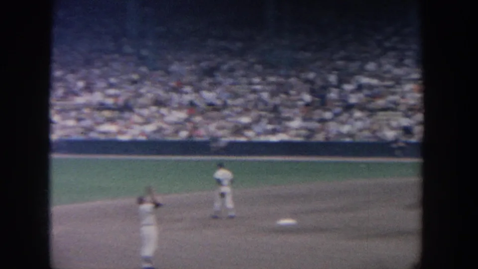 1964 New York baseball frame showing one player with raised arms on the infield and another player positioned farther back.