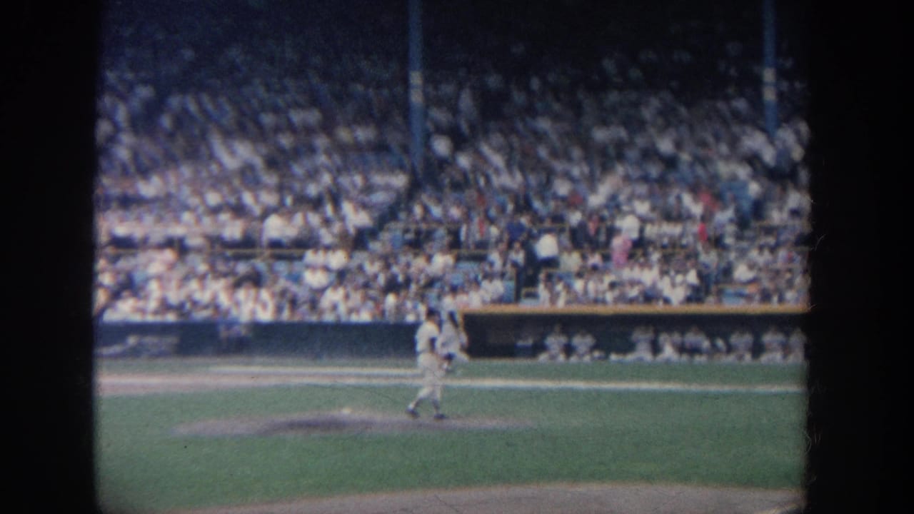 Baseball player stands near the mound area with a full grandstand in the background.