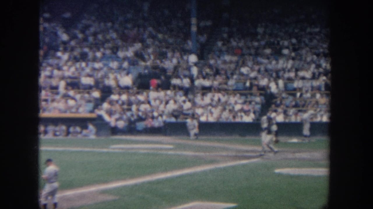 1964 New York home-movie view of a baseball game from the stands, with players near the plate and a dense crowd beyond the infield.
