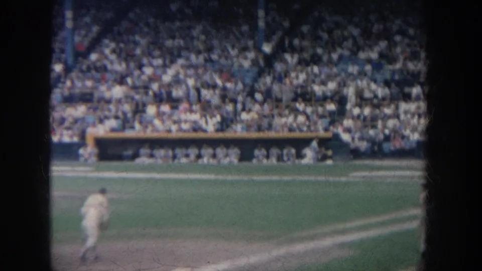 1964 New York baseball frame showing a player running across the infield as the dugout and crowded stadium seating remain in the background.