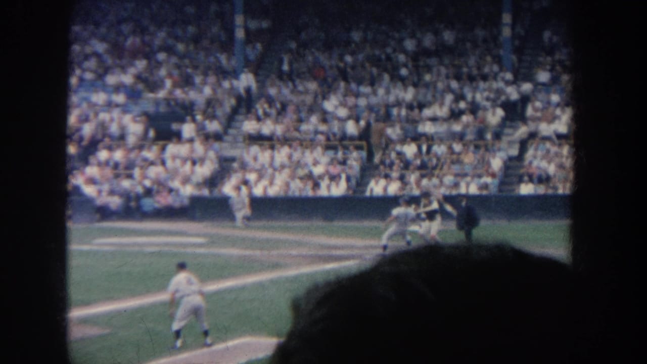 1964 New York baseball game viewed from the stands, with the batter at home plate and spectators filling the grandstand beyond.