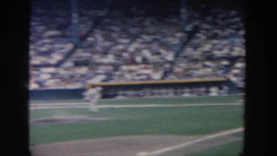 Motion-blurred 1964 New York baseball field view showing a player moving across the infield as the crowd sits beyond the wall.