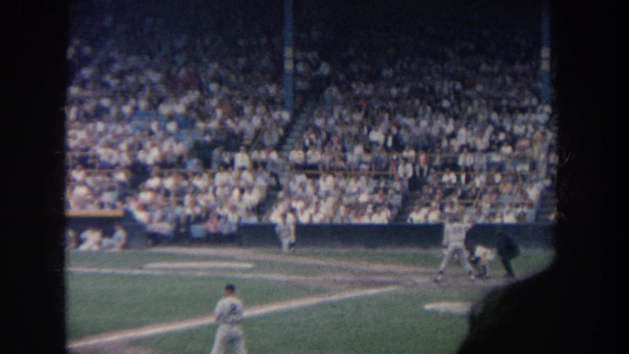 Batter, catcher, and umpire near home plate with a fielder in the foreground and full stands beyond.