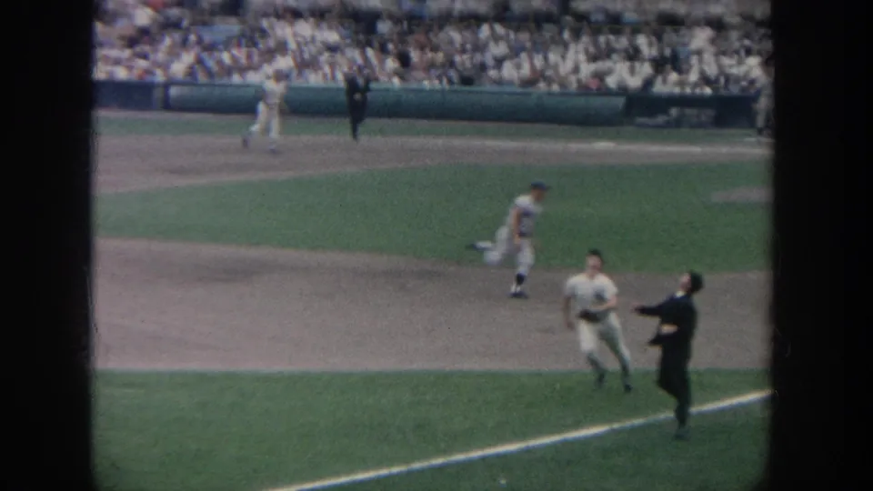 1964 New York baseball home movie showing players moving near the infield and an umpire on the foul line, with a packed crowd behind them.