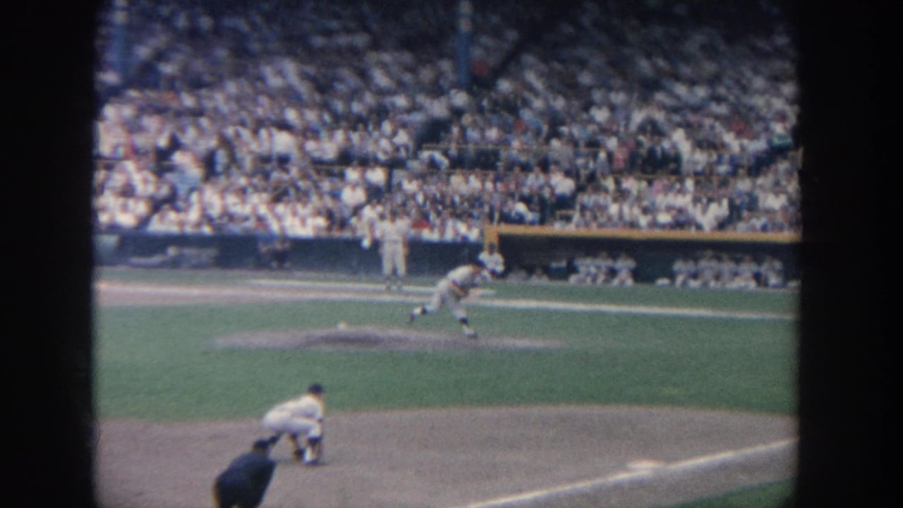 Pitcher throws toward home plate as the batter waits in a crowded stadium.