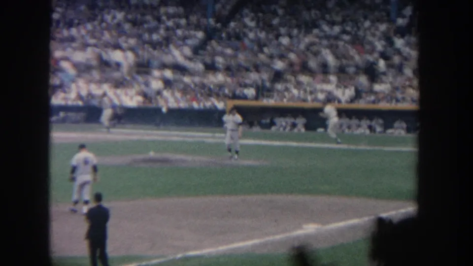 1964 New York home-movie baseball frame with players moving near the baselines and a full stadium visible behind the infield.