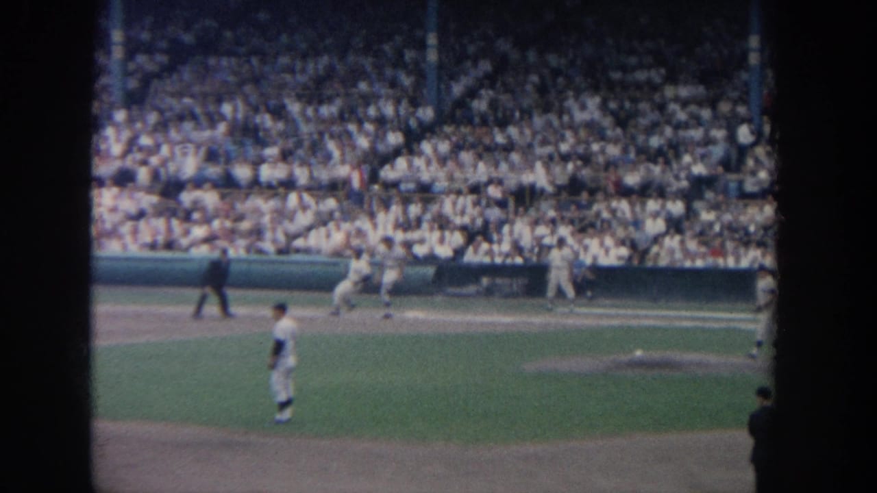 1964 New York baseball game viewed from the stands, with players on the field and a dense crowd in the background.