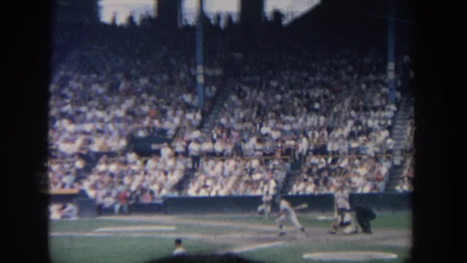 A baseball batter appears near home plate during a 1964 New York stadium game, with spectators filling the background.