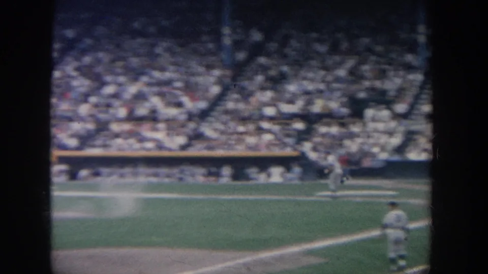 Late-frame 8mm view from the stands at a 1964 New York baseball game, showing a player near the line and a packed stadium beyond.