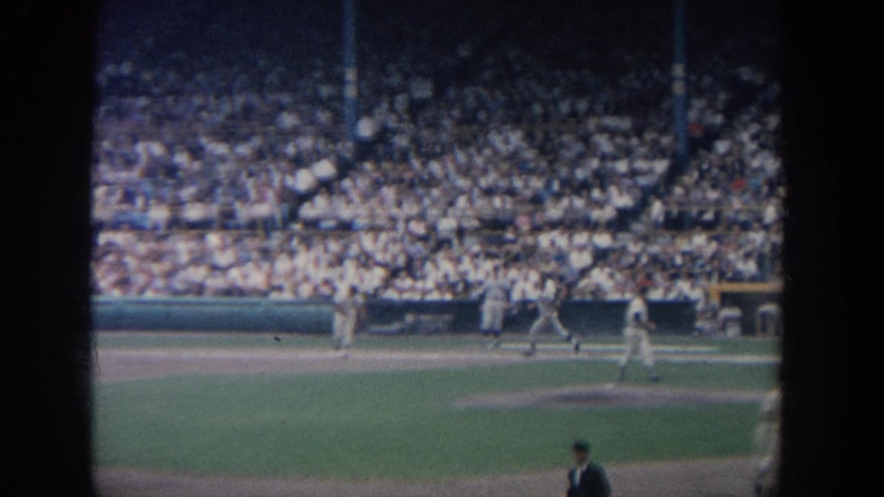 Several baseball players stand near the infield with spectators in the stands.