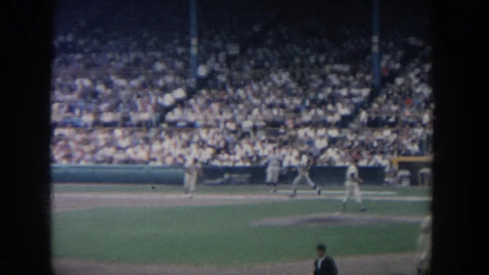 Wide home-movie angle of a 1964 New York baseball game with players near the infield and a crowded grandstand.