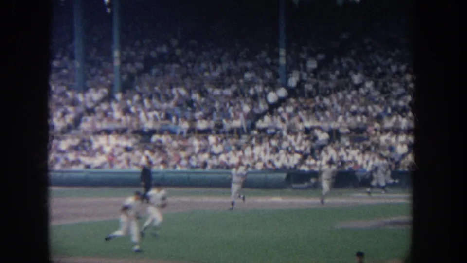 Spectator-shot 8mm frame of players moving along the base path during a 1964 New York baseball game.