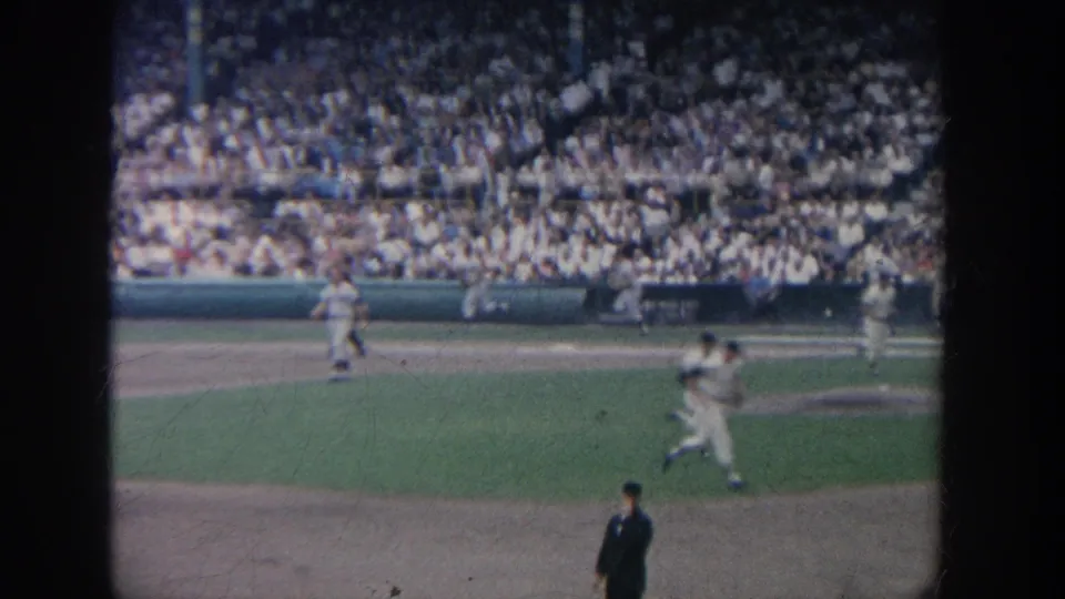 1964 New York home-movie view of a baseball play in motion, with players and packed stands visible.