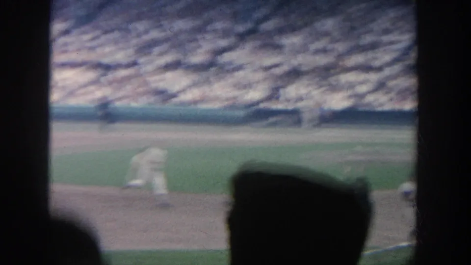 1964 New York 8mm view of a baseball game from the stands, partly obscured by dark foreground spectators and stadium framing.
