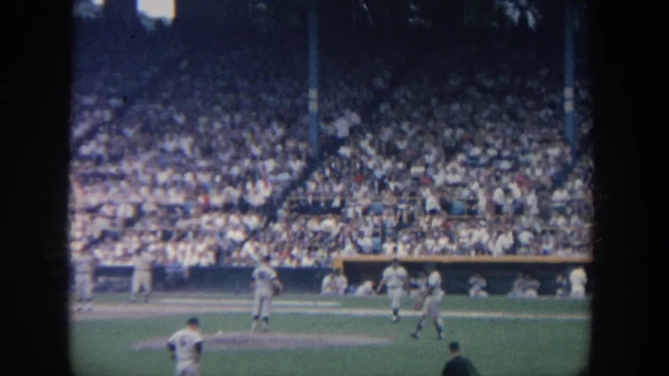 1964 New York 8mm stadium view with several baseball players on the field and a dense crowd in the background.
