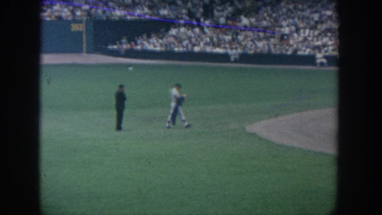 1964 New York 8mm stadium baseball view with players on the green field and a crowded grandstand in the background.